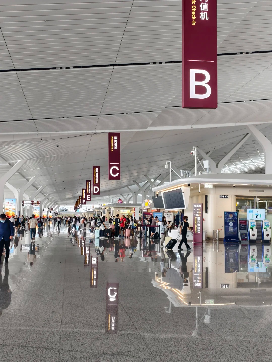 Check-in hall at Xi'an Xianyang T5, with lettered zone signs B, C, D, E, F and G hanging above the islands