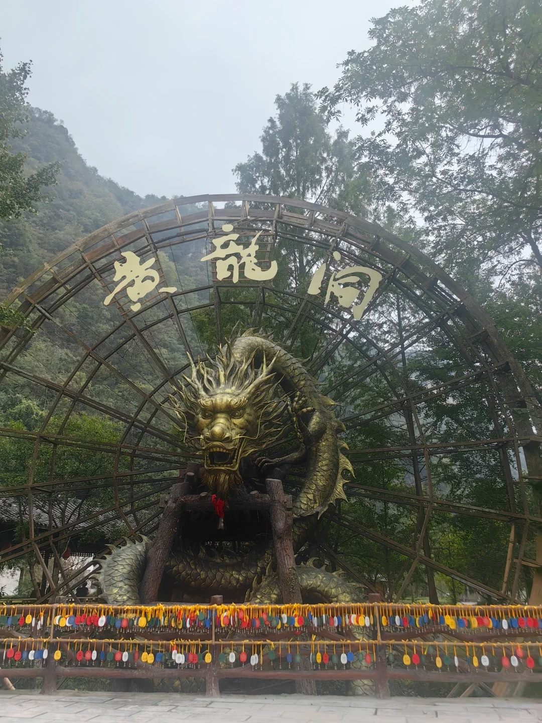 The entrance display at Yellow Dragon Cave, Zhangjiajie: a large wooden water-wheel frame carrying the Chinese characters for Huanglong Dong in gold, with a golden dragon sculpture beneath it.
