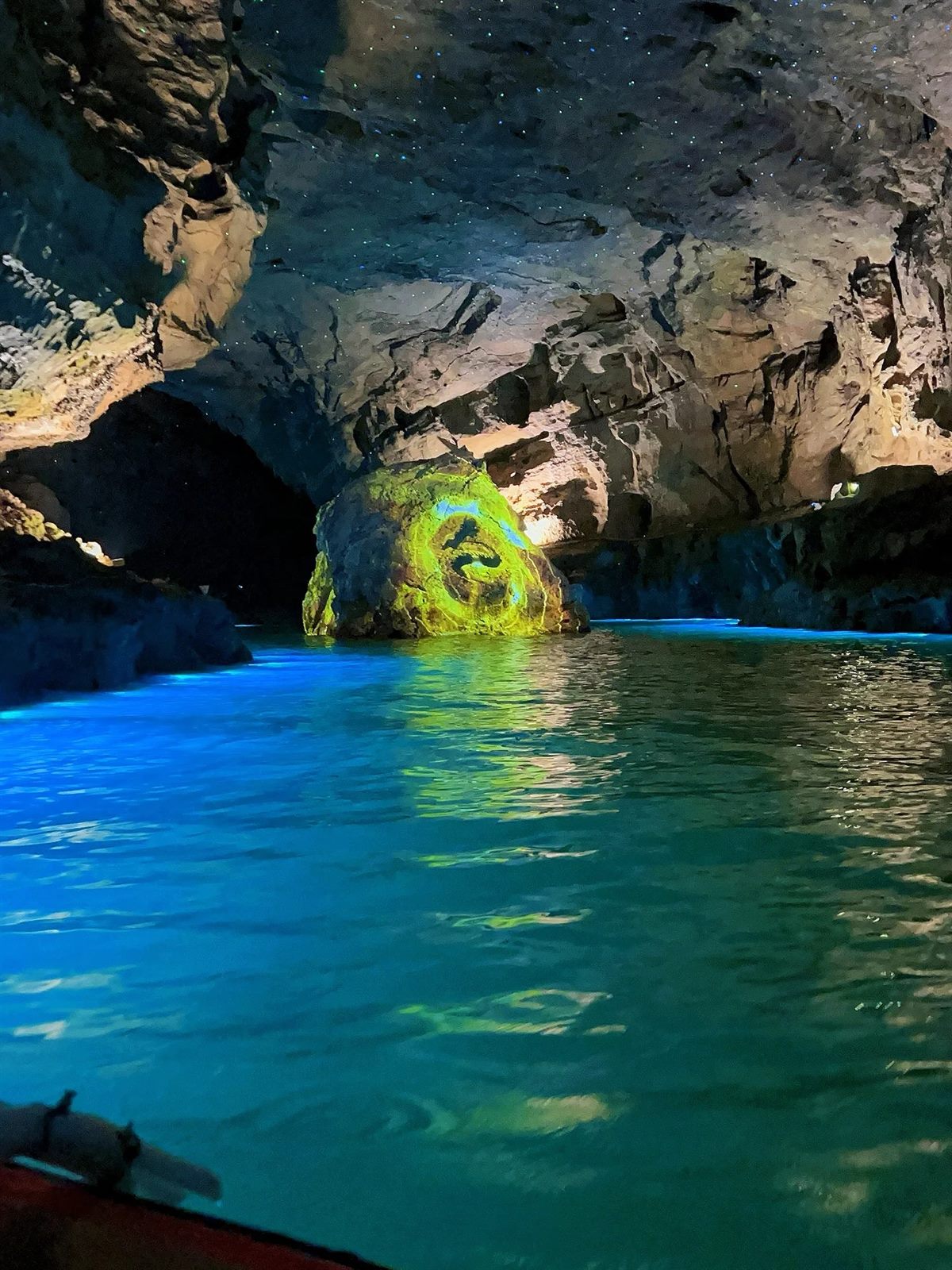 The underground river inside Yellow Dragon Cave, Zhangjiajie, seen from a boat: turquoise-lit water, a rock lit in yellow, and a projected star field across the cave ceiling.