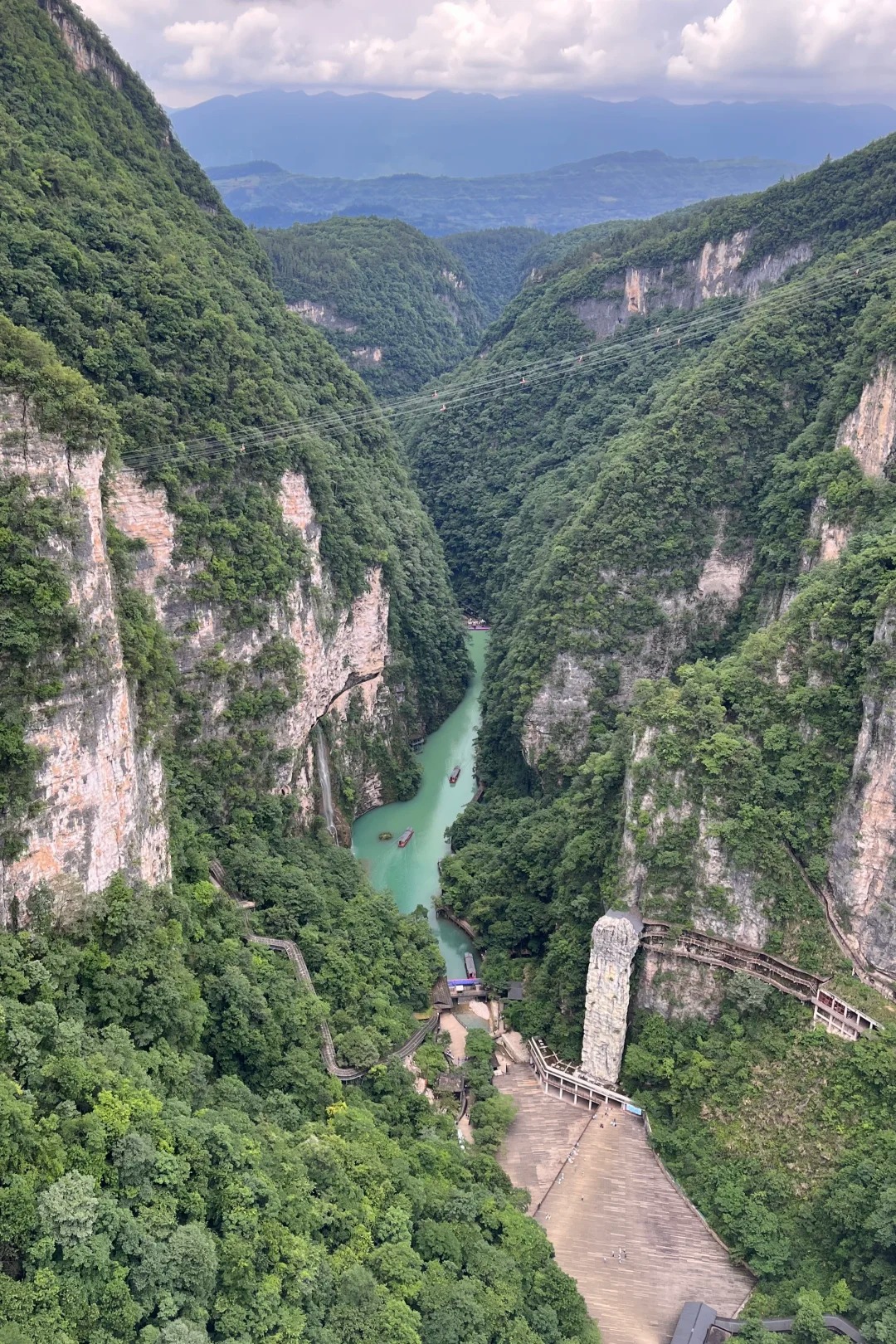 The Zhangjiajie Grand Canyon from above: the jade-green river and tour boats on the floor, the zip-line cables crossing overhead, and the Yixiantian cliff area lower right.