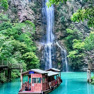 A wooden sightseeing boat on the jade-green Shenquan Lake below a waterfall, at the exit end of the Zhangjiajie Grand Canyon.