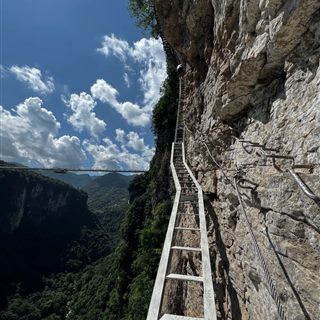 The via ferrata iron-rung course traversing the cliff face, with the glass bridge spanning the canyon behind.