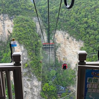 The zip line crossing the Zhangjiajie Grand Canyon beside the glass bridge, with the descent slides visible on the canyon floor below.