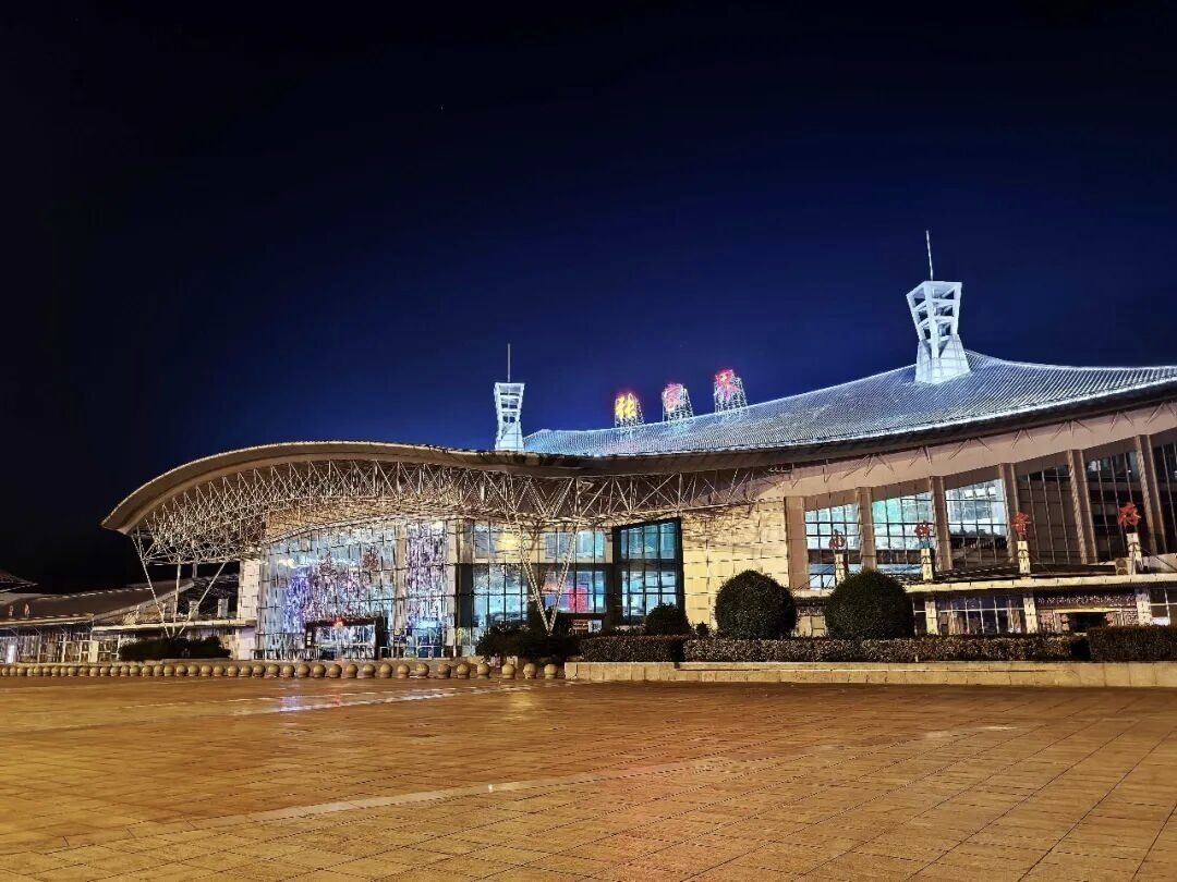 The curved, illuminated roof of the central Zhangjiajie Station at night, with its station-front plaza.